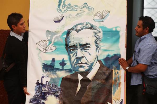 Dos jóvenes sostienen una pintura donde aparece Juan Rulfo. Foto: Agencia EFE
